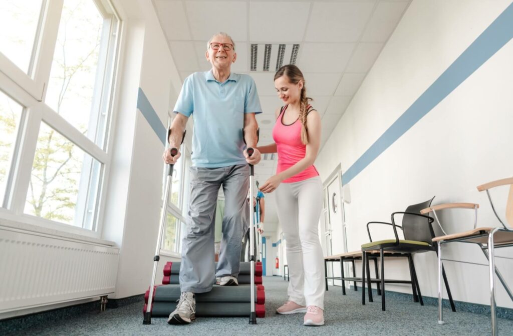 A physiotherapist helps their older adult patient walk over obstacles using a mobility device as part of their injury recovery.