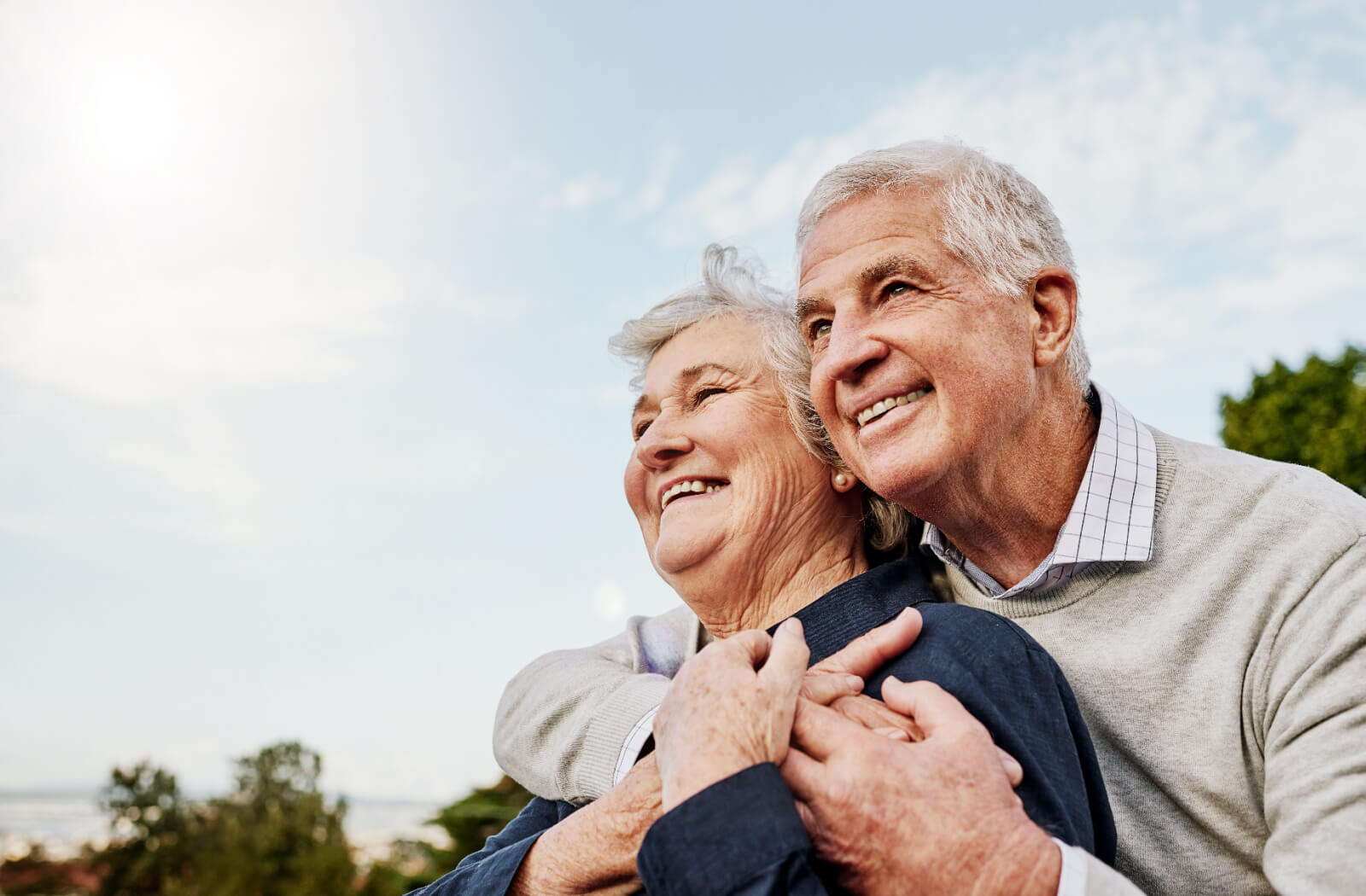 An older couple smiles while hugging one another and looking up at the sky