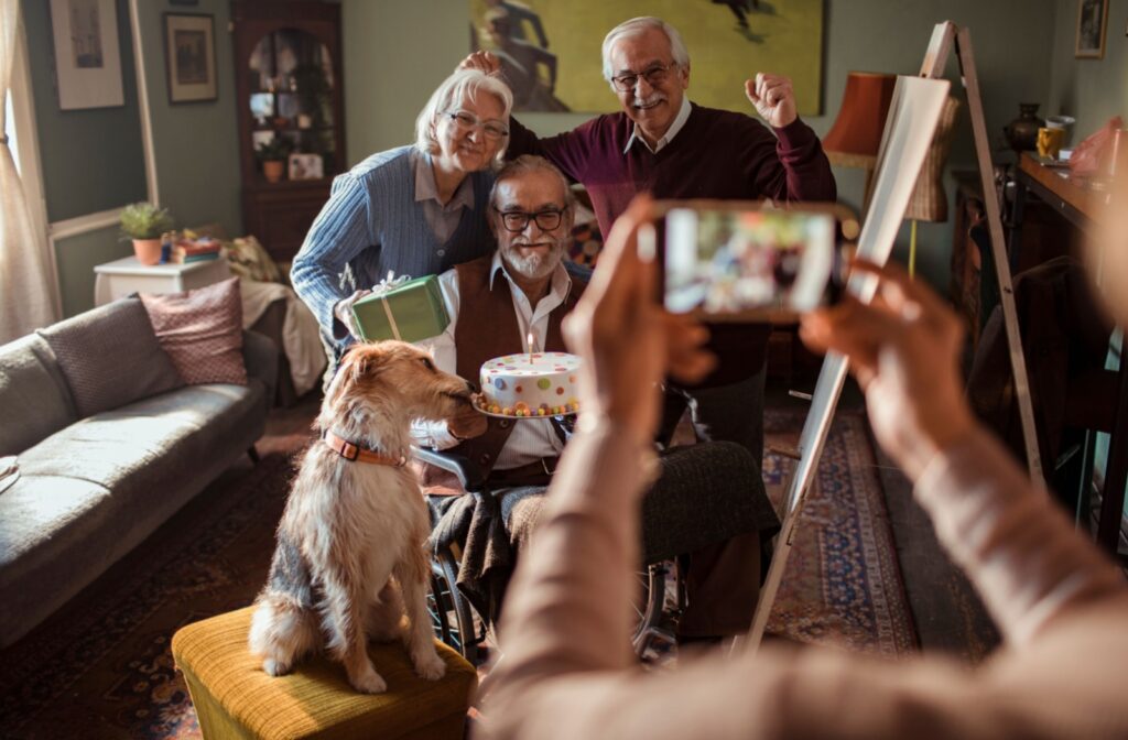  A dog licks a birthday cake while a photo is taken of a group of older adults celebrating at an independent living community